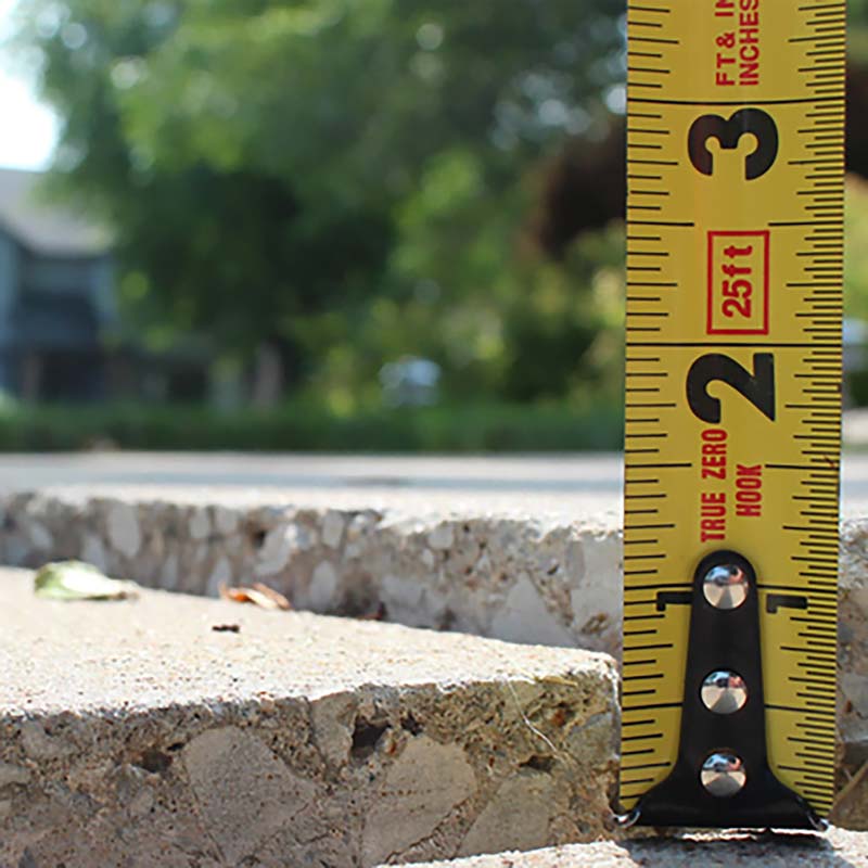 Sidewalk with dropped slab and ruler showing depth of drop